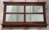 Front view of a rectangular mirror divided into four panels by a solid wood frame with five hooks attached on the bottom ledge.