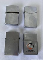 Four metal lighters laid out in a 2x2 arrangement showing fronts and hinged tops, one with company logo Northern Helicopters Ltd.