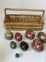 Photo of all eight decorative eggs and basket, showing variation in materials and sizes.