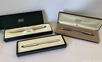 Three Cross writing instruments in original boxes showing two pens and one mechanical pencil with silver-tone finishes.