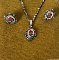 Close-up photo of necklace and earrings showing detailed miniature floral embroidery in metal frames.
