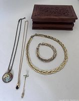 Photo showing the braided gold-tone necklace and matching bracelet, globe pendant necklace, black stone necklace, peridot bow and arrow pin, and wooden box