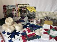 Photo showing yarn balls, assorted quilting squares, pattern books, and fabric pieces on a white surface
