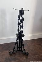 Full view of the black wrought iron plant stand showing twisted vertical rods and curled feet base.