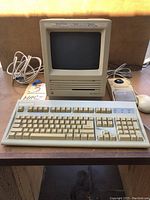 Full view of Macintosh SE desktop with keyboard and mouse placed on desk, showing cables at the back.