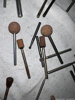 Photo showing close-up of various Dremel bits with brown abrasive heads and metal shanks on white fabric background.