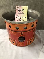 Front and top view showing round orange HeatPal 5000 grill with control knob and ventilation holes, features a sticky note indicating propane gas.