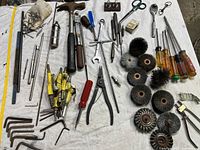Full view of the tool collection showing wire wheel brushes, various screwdrivers, Allen wrenches, hammers, pliers, and other hand tools on a white surface.
