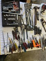 Wide view of assortment of hand tools on white cloth: socket set, wrenches, screwdrivers, hammer, pliers