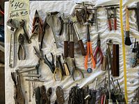 Photo showing various hand tools laid out including adjustable wrenches with wooden handles, clamps, pliers with colored handles, and wire cutters.