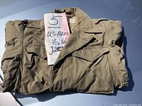Folded vintage US Army field jacket in olive drab green color with a sign showing lot number 5