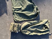 Photo of group showing large green canvas sea bag marked with 'US' and military duffel bag on pavement