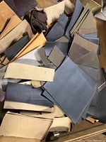 Photo showing mixed assortment of sandpaper sheets in various sizes and colors including gray, brown, and tan stacked loosely.