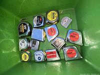 Photo showing 17 tape measures in a green container, displaying varied colors, sizes, and brands.
