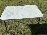 Full view of vintage rectangular dining table with green and white marbled Formica top, set outdoors on grass.