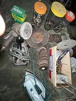 Top down view showing vintage electric sander, General Electric iron, jars of nuts and bolts, and stacks of sanding discs and grinding discs.