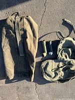 Photo showing two olive drab canvas military sea bags with attached straps and two vintage flashlights placed beside them on pavement.