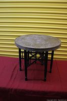 Antique folding wooden table with brass top facing forward with legs extended.