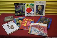 Photo showing the front covers of 9 art-related books arranged on a red surface with a yellow background shutter.