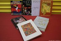 Seven art and fashion books arranged on red surface against yellow shutter background.