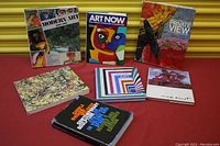 Set of 8 art books arranged in two rows on a red surface with a yellow background, showing colorful covers with modern and abstract art styles.