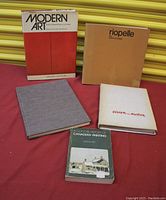 Five art books on a red surface with a yellow background, showing titles and covers of each book.