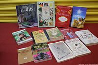 Twelve books laid out on a red surface, titles related to herbs, healing, and health.