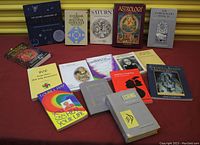 Wide view of 14 books focused on astrology, healing, and spirituality arranged on a red surface.