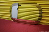 Photo showing the full oval-shaped double layer mirror with clear center and smoked outer border, resting against a yellow corrugated background.