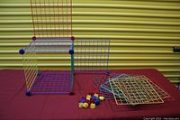 Set of colorful wire grid panels and corner connectors arranged as a small cube and separate panels resting on table.