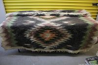 Full view of thick wool blanket spread out on a surface showing large central diamond geometric pattern in earthy tones.