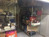 Two side-by-side chrome wire shelving racks loaded with books and boxes inside a metal storage unit