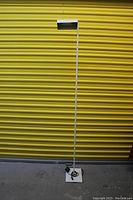 Full view of the tall white post modern minimalist floor lamp against a yellow background.