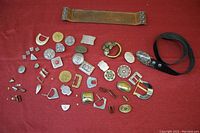Full assortment of belt buckles and wide leather strap laid out on a red fabric background.