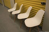 Front view of four chairs in a row against yellow background, showing white seats, wood legs and metal supports.