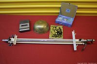 Overview of the lot showing the brass singing bowl, measuring instrument, abstract art and small box on red fabric background