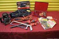 Overview of tool lot items on red table including router, extension cords, clamps, hacksaw, organizer box, and sander.