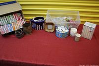 Wide shot of lot including fabric dye boxes, pottery items, candles, and container of lighting fixture crystals