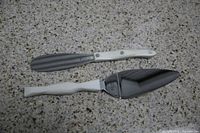 Two Cutco cake knives with white ribbed handles and stainless steel blades placed on a light granite surface.