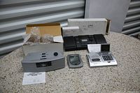 Photo showing six assorted clock radios and digital alarm clocks and accessories arranged on a stone-like surface, some with foam or bubble wrap packaging.