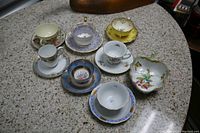 Seven demitasse tea cups with saucers and one fruit-shaped decorative candy dish displayed on a countertop.
