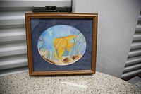 Framed watercolor painting showing a yellow fish underwater with aquatic plants in the background.