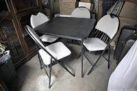 Vinyl topped square folding table surrounded by four white padded folding chairs in storage area