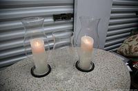 Three glass globe candle holders on a round, speckled stone table, two with battery-operated white candles lit inside, one empty. The candle holders have black ring bases. The photo shows size and shape clearly.