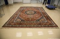 Full view of large oriental-style carpet laid on showroom floor, showing medallion pattern, red field, navy border, fringed ends