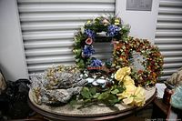 Photo of multiple seasonal wreaths and decor items on a table showing various artificial floral and natural element decorations.