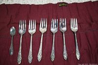Six forks and one small spoon arranged on a red fabric roll with a Birks label