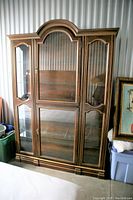 Front view of the wood and glass china cabinet showing glass doors, shelves, and lighting feature.