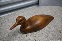 Photo of the wooden carved duck showing smooth polished body and detailed head and beak, placed on a speckled surface.