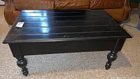 Front view of black painted coffee table with turned wood legs and some scratches visible on the surface.